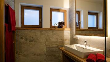 Un baño con pared de piedra, tocador de madera, lavabo blanco y espejo.