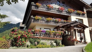 A multi-story building with balconies adorned with colorful flowers, a stone facade, and a wooden entrance.
