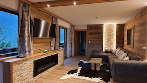 A cozy living room with a stone fireplace, a large flat-screen TV, a sectional sofa, and a cowhide rug.