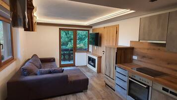Una sala de estar moderna con un sofá, una cocina con armarios de madera y un ventanal con vistas a zonas verdes.