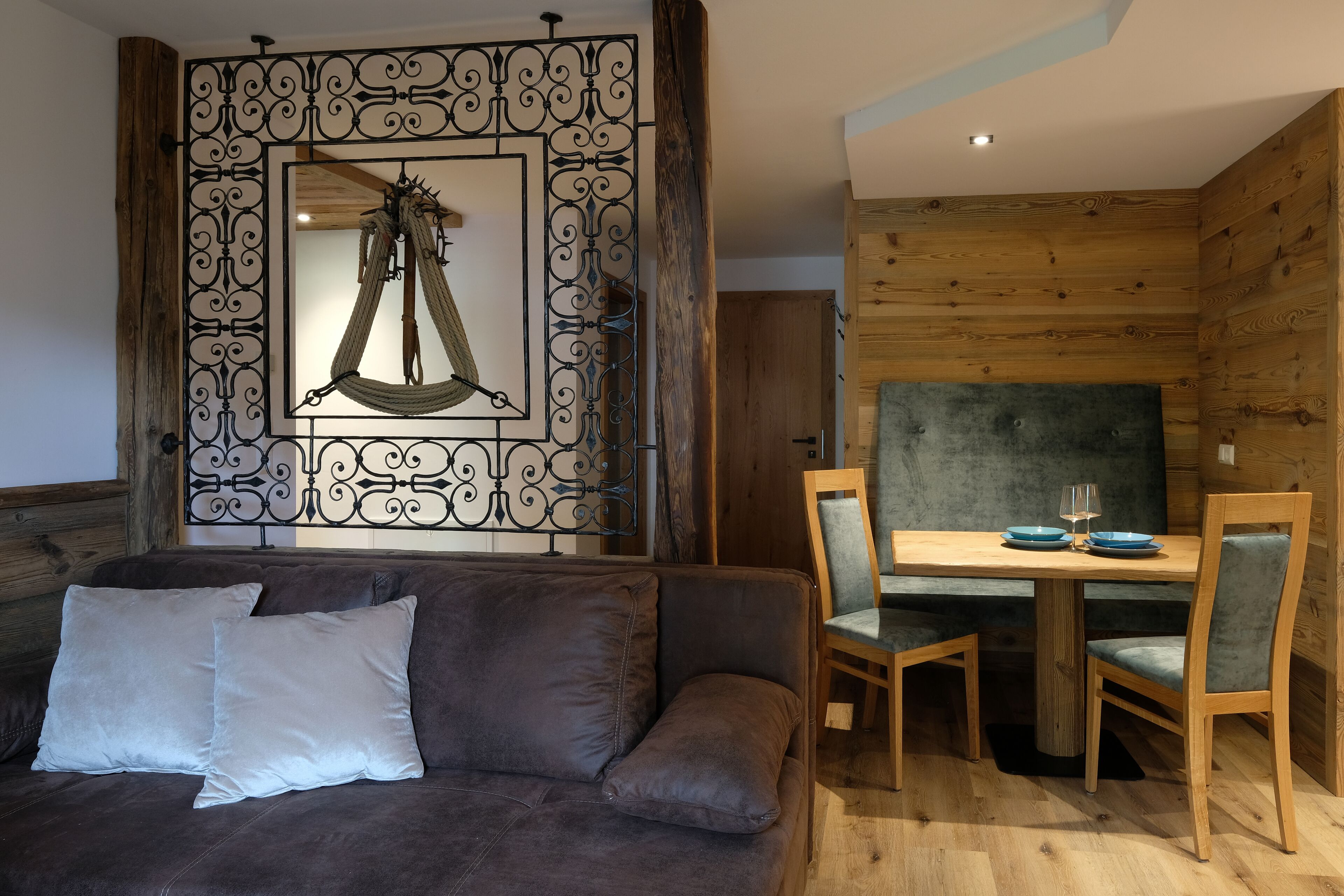 A cozy room with a brown leather sofa, a wooden dining table with chairs, and a decorative metal partition with a hanging hammock.