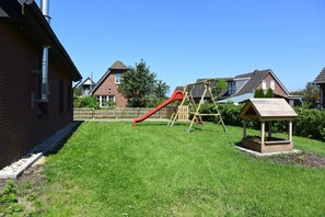 A residential backyard with a red slide, a wooden swing set, and a small wooden structure.