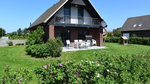 Een tweelaags huis met een balkon, een terras met tuinmeubilair en een verzorgde tuin met bloeiende planten.