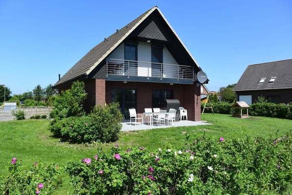 A two-story house with a balcony, a patio with outdoor furniture, and a well-maintained garden with flowering plants.