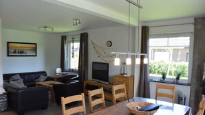 Een moderne woonkamer met een houten eettafel, een zwart leren bank en een flatscreen televisie.
