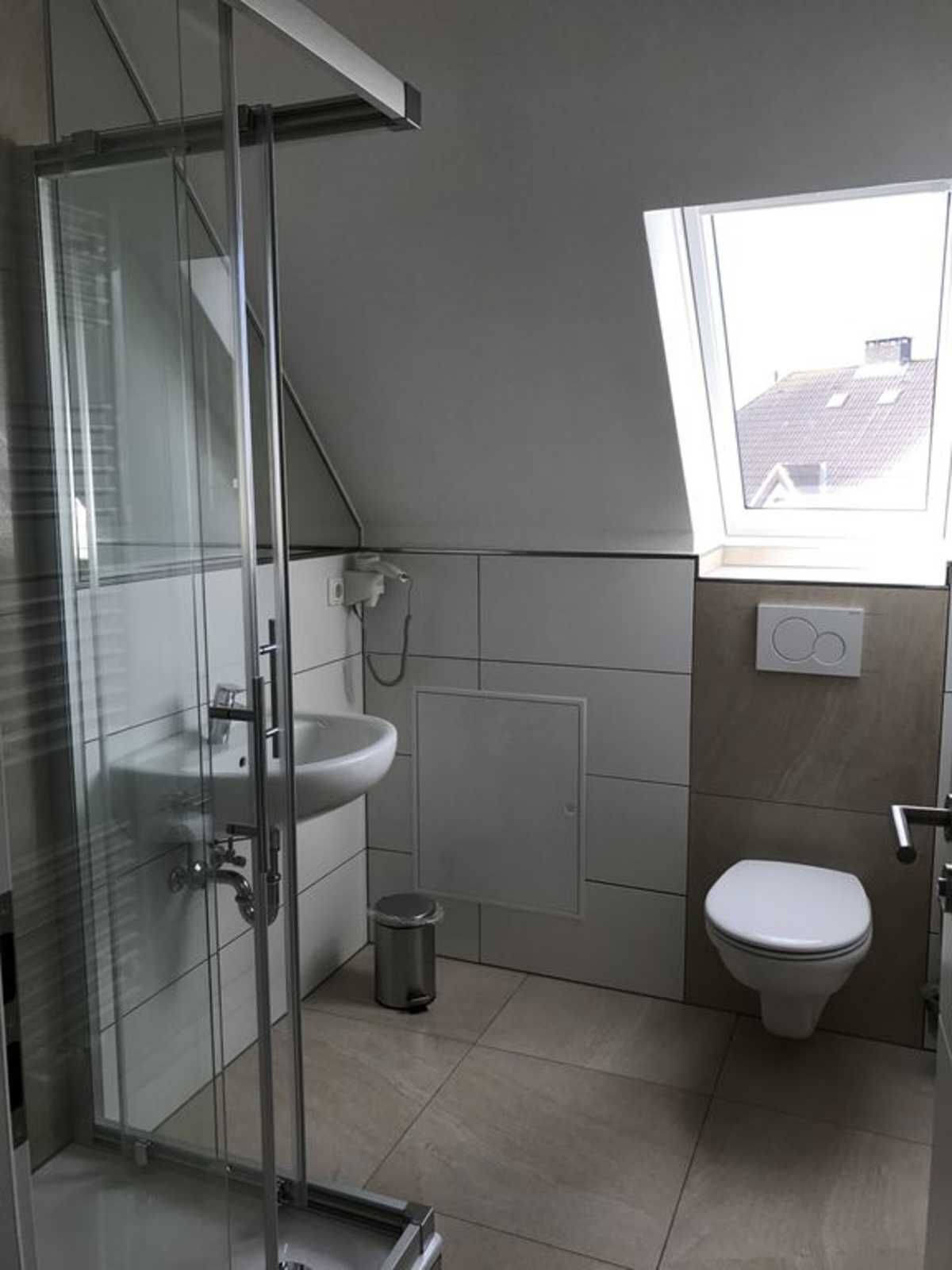 Ein modernes Badezimmer mit Duschkabine aus Glas, Waschbecken, Toilette und einem Fenster für Tageslicht.