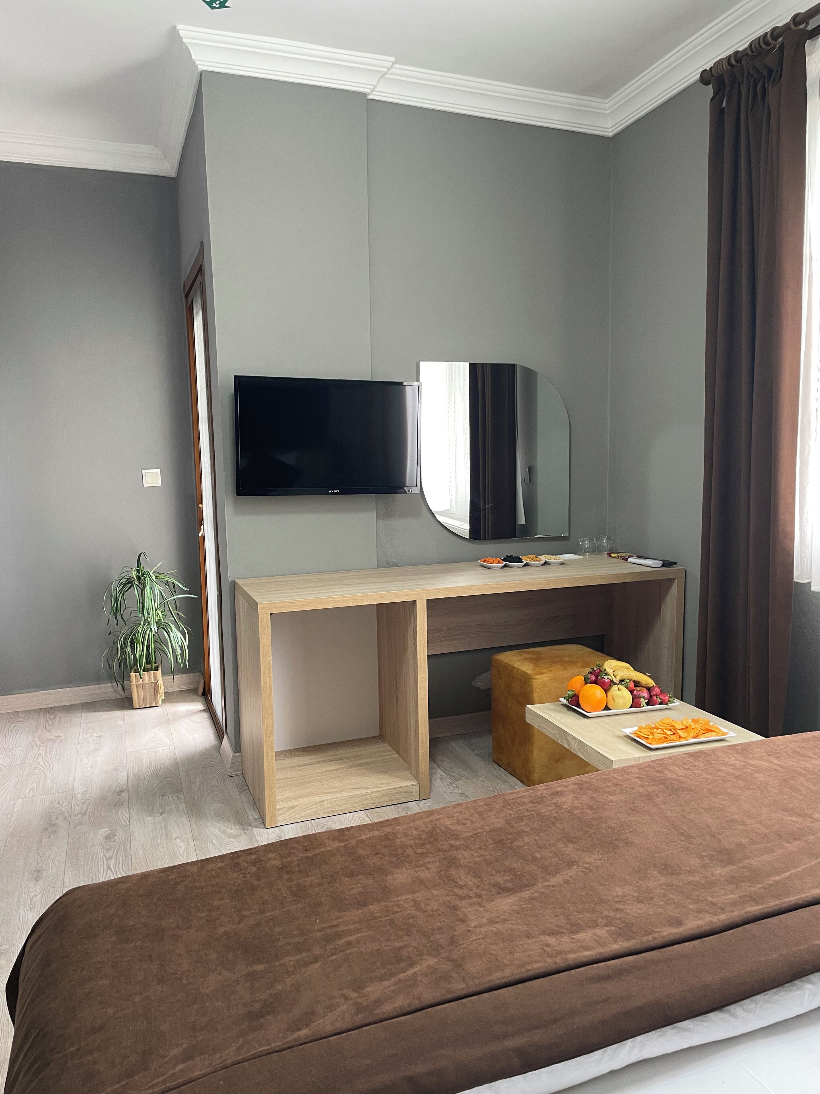 Ein modernes Hotelzimmer mit einem Bett, einem Holztisch, einem Flachbildfernseher, einem Spiegel und einer kleinen Topfpflanze.