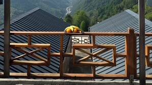 Una terraza de madera con baranda de metal que da a un valle con río y colinas.