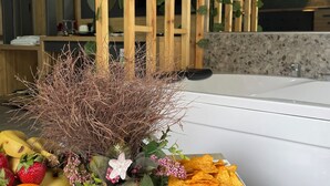 Una mesa con frutas, flores y patatas fritas en una habitación moderna con un separador de madera y una bañera.