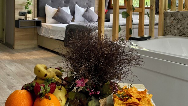 Un dormitorio con cama, mesitas de noche y una mesita auxiliar. Hay una planta decorativa y una bandeja de frutas sobre la mesa.