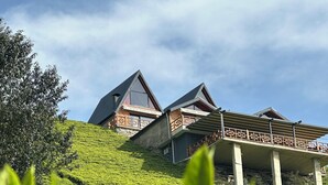 Un albergue de montaña con un techo empinado y balcones de madera, rodeado de abundante vegetación.