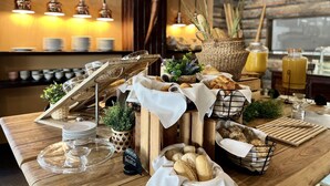 Un buffet de petit-déjeuner comprenant du pain, des viennoiseries et un distributeur de jus de fruits.