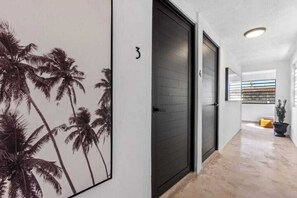 A hallway with a door marked with the number 3, a potted plant, and a view of a balcony with a railing. - Junior Suite Steps To Loiza Street & Best SJ Beach (San Juan)