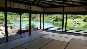 A traditional Japanese room with tatami flooring, large windows, and a view of a serene pond.