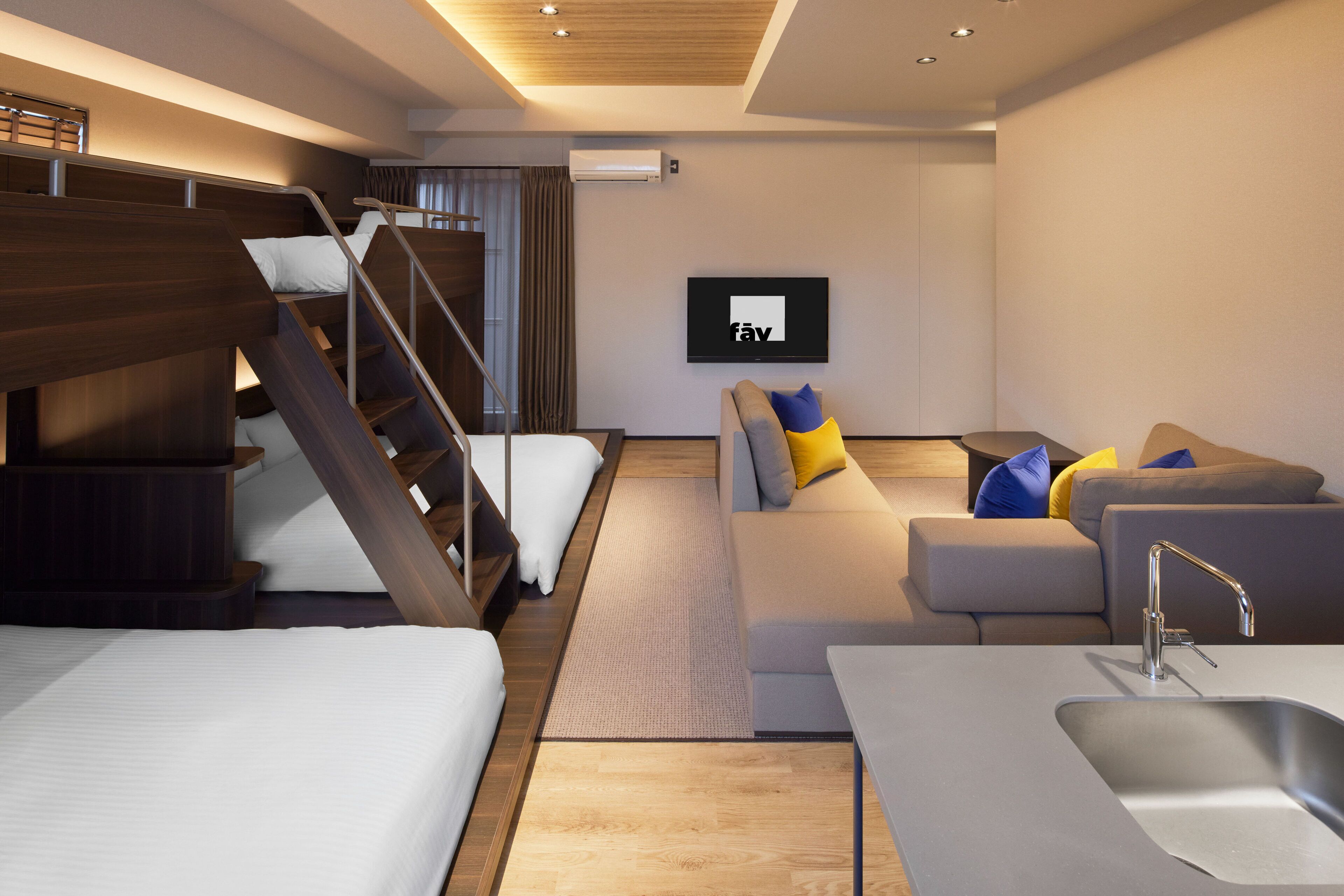 Una habitación de hotel moderna con una escalera, un conjunto de sofás, un televisor de pantalla plana y una zona de cocina.