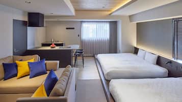 Een moderne hotelkamer met een bank, twee eenpersoonsbedden, een kleine kitchenette en een groot raam met gordijnen.