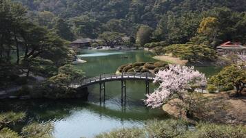 A serene landscape with a bridge over a calm lake, surrounded by lush greenery and traditional architecture.