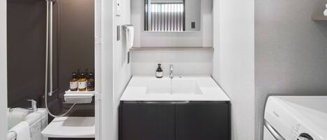 Un baño pequeño con ducha, lavamanos y lavadora integrada.