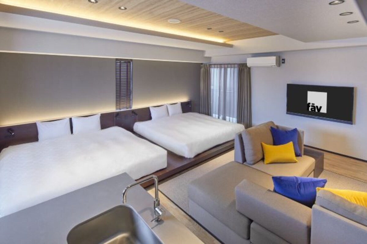 Una habitación de hotel moderna con dos camas, un sofá, un televisor y un lavamanos.