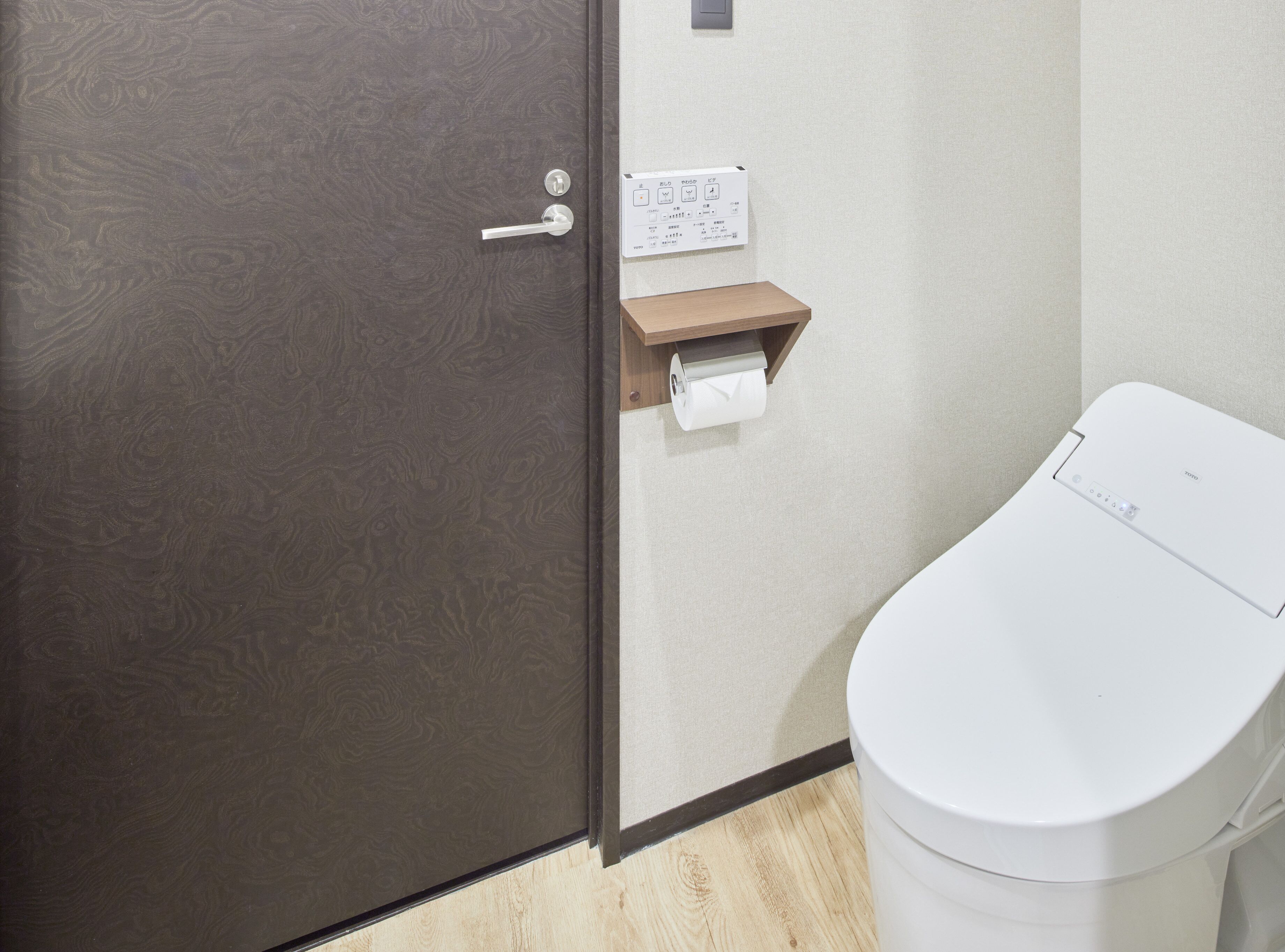 Un baño con inodoro, dispensador de toallas de papel y panel de control en la pared.