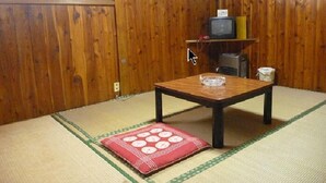 Ein traditioneller japanischer Raum mit Tatami-Böden, einem niedrigen Holztisch, einem Fernseher auf einem Regal und einem Kleiderständer.