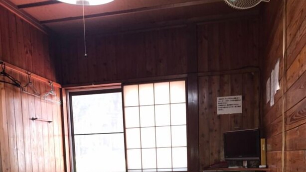 Ein Zimmer mit Holzwänden, einem Tatami-Boden, einem Tisch, einem Fernseher und einem großen Fenster mit Blick.