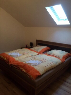 A single bed with a wooden headboard in a room with a sloped ceiling and a skylight.