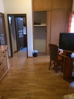 Una habitación con piso de madera, un escritorio con silla, un televisor y un armario.