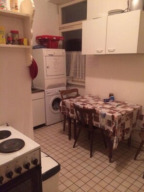 A compact kitchen with a stove, a table with chairs, a washing machine, and a small window with a curtain.