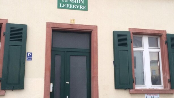 Un bâtiment avec une porte et des volets verts, portant l’inscription « Pension Lefebvre ».