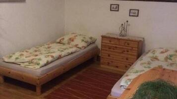 Une petite pièce chaleureuse, dotée d’un plancher en bois, d’un lit simple avec une literie à motifs floraux, d’une commode en bois et d’une petite table sur laquelle est posée une plante.