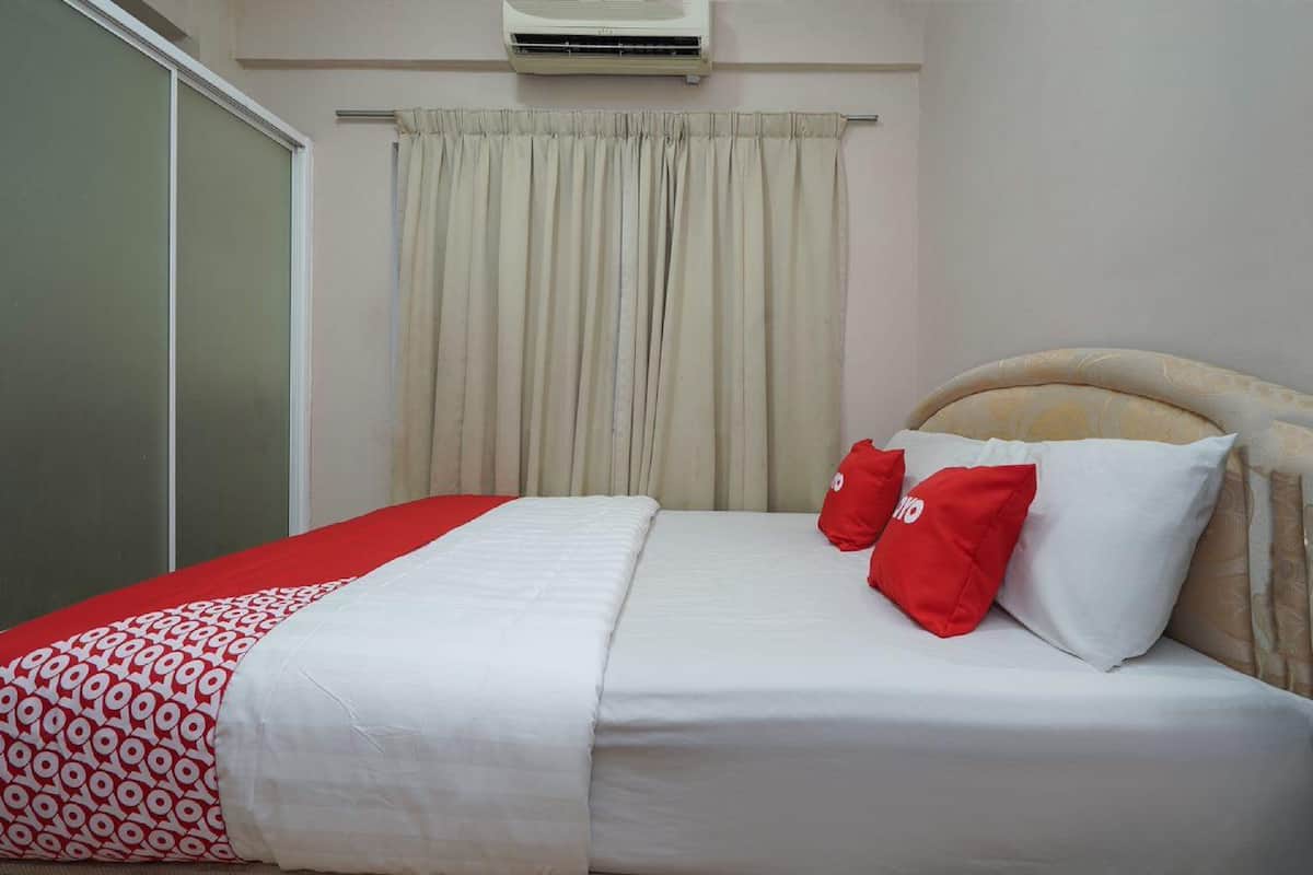 A hotel room with a bed, a window with curtains, and an air conditioning unit on the wall.