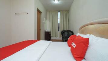 A hotel room with a bed, a red pillow, a chair, and a window with curtains.