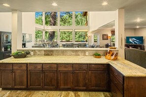 A spacious kitchen with a large island, wooden cabinets, and a view of the outdoors through large windows.