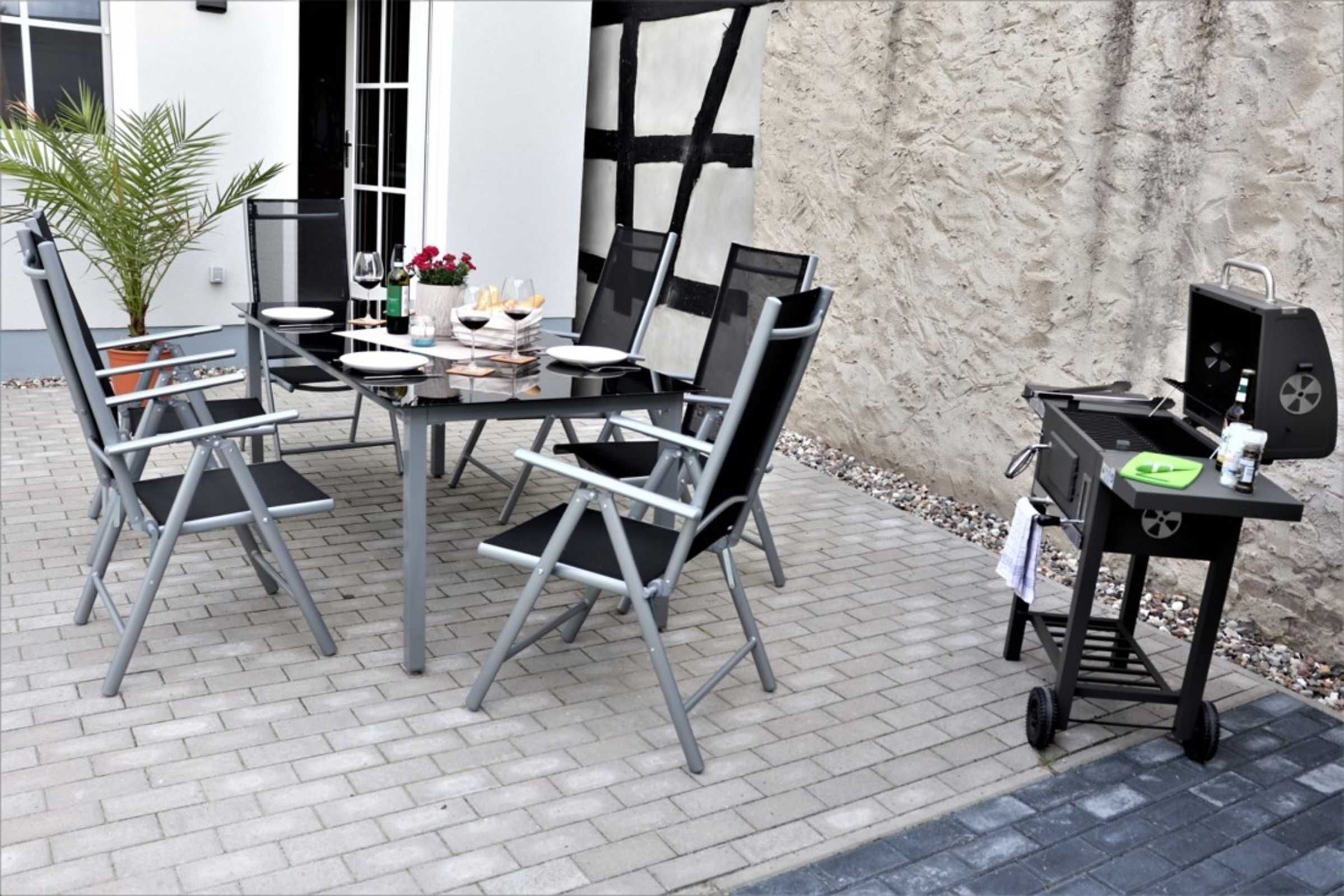 An outdoor patio with a table set for dining, chairs, a grill, and a potted plant.