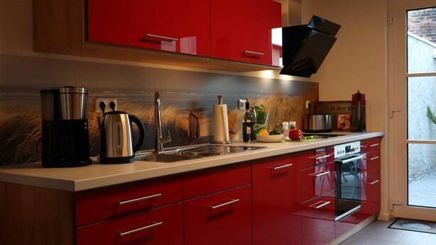 A modern kitchen with red cabinetry, stainless steel appliances, and a large window.