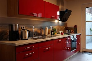 A modern kitchen with red cabinetry, stainless steel appliances, and a large window.