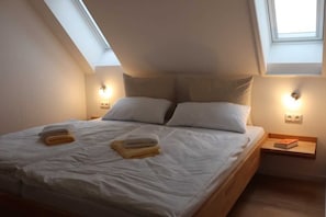 A bedroom with a skylight, two bedside tables, and a bed with pillows and folded towels.