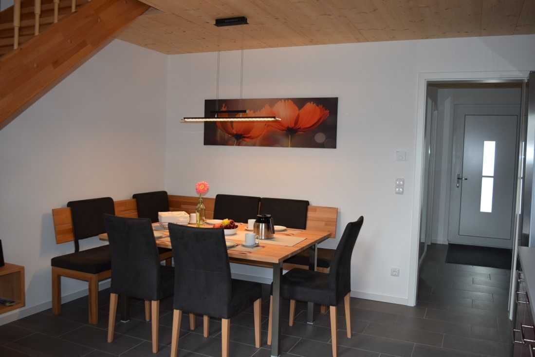 A dining area with a wooden table and chairs, a painting on the wall, and a staircase.