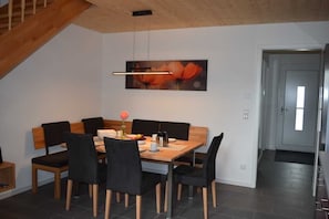 A dining area with a wooden table and chairs, a painting on the wall, and a staircase.