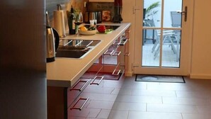 A modern kitchen with a large window, a door leading to an outdoor area, and a tiled floor.