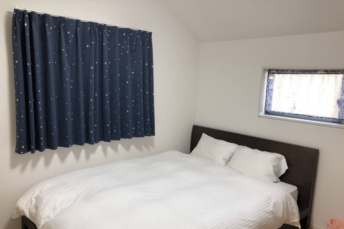 A single bed with white bedding in a room with a dark blue curtain featuring a star pattern.