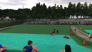 A playground with children playing on a green turf surface, surrounded by a fence. - Tokyo Toneri Garden House-Stay (Tokyo)