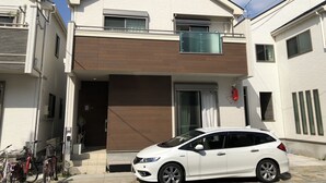 A two-story residential building with a white exterior, a balcony, and a white car parked in front. - Tokyo Toneri Garden House-Stay (Tokyo)
