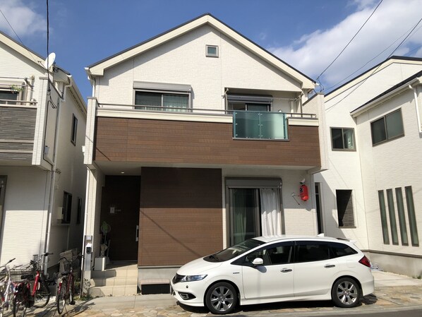 A two-story residential building with a white exterior, a balcony, and a white car parked in front.
