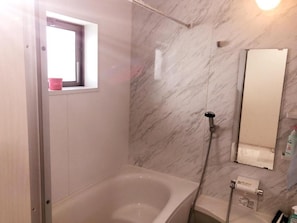 A bathroom with a bathtub, a shower, a window, and a mirror.