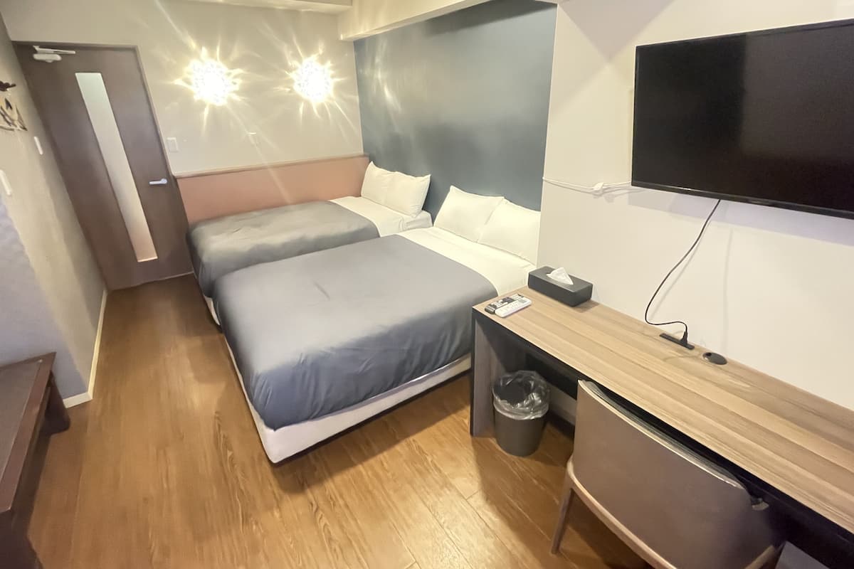 Ein modernes Hotelzimmer mit zwei Betten, einem Schreibtisch, einem Fernseher und einem Papierkorb.