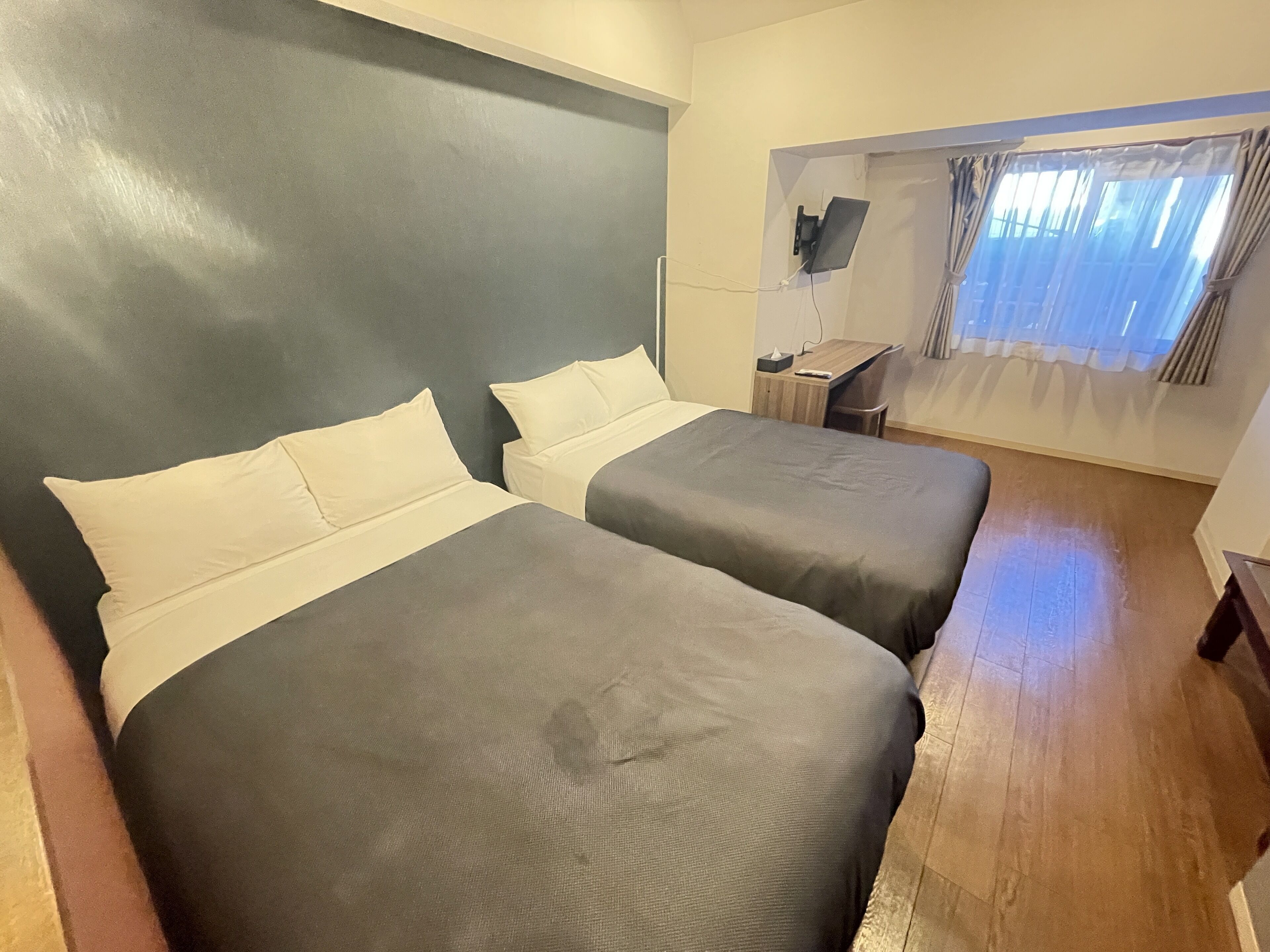 Hotellihuone, jossa on kaksi sänkyä, työpöytä, tuoli ja ikkuna, jossa on verhot.