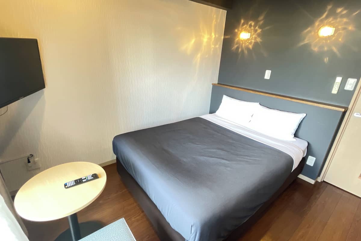 Ein Hotelzimmer mit einem Bett, einem kleinen runden Tisch mit Fernbedienung und einem an der Wand montierten Fernseher.