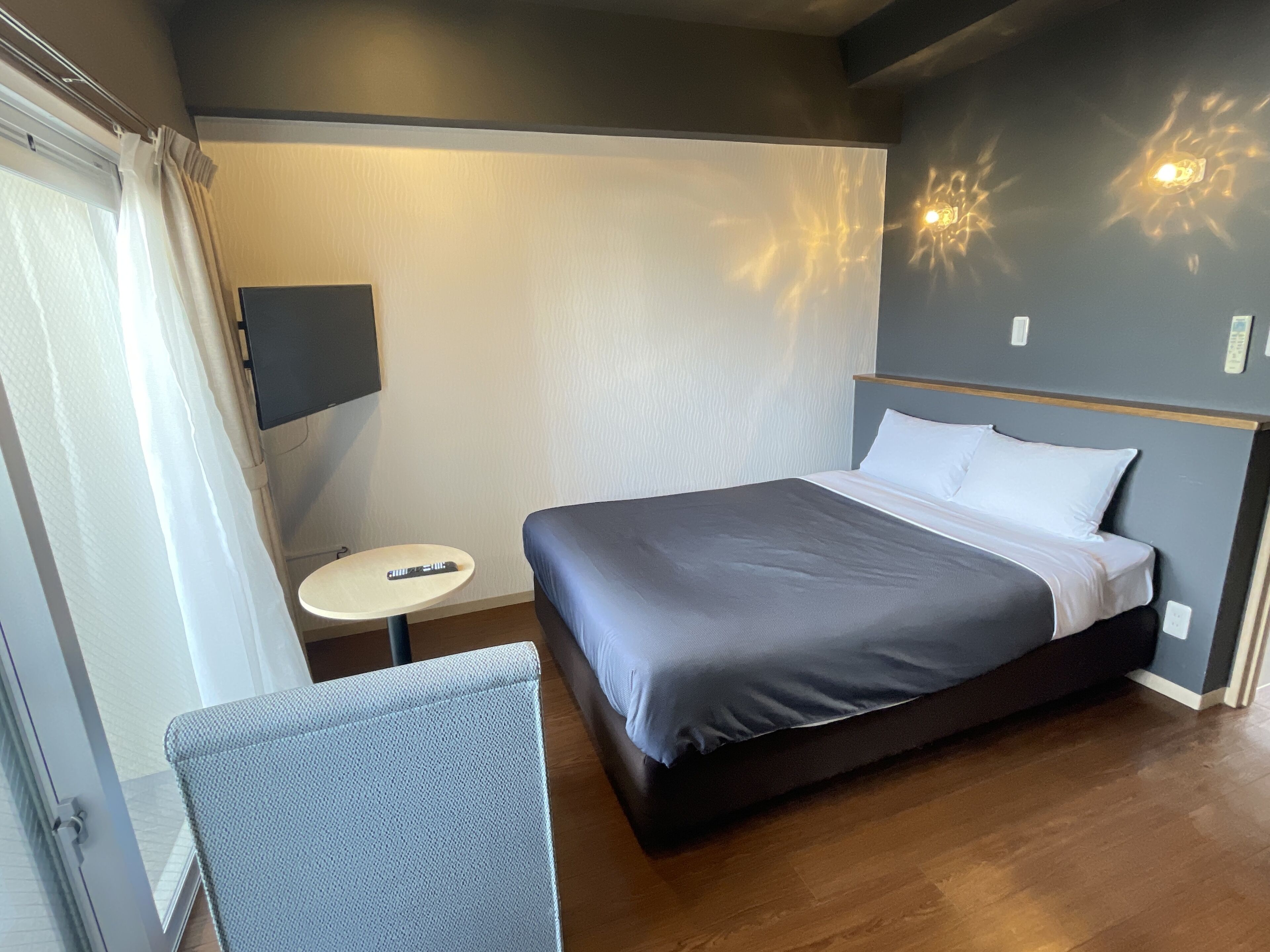 A modern hotel room with a large bed, a small round table, and a TV mounted on the wall.